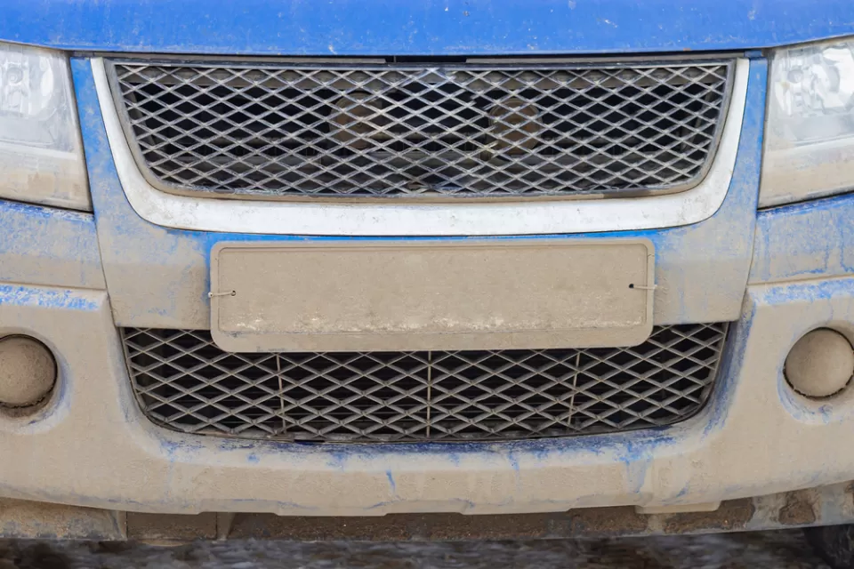 Close-up of license plate on blue car covered in mud, license plate is unreadable.